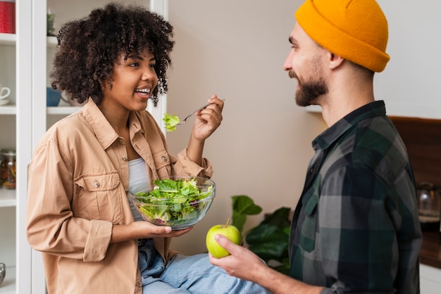 Man holding apple and looking at woman eating salad