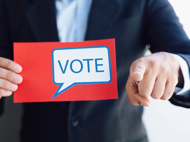 Free photo man holding a ballot and pointing to the camera