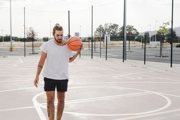 Мужчина держит баскетбол в открытом дворе