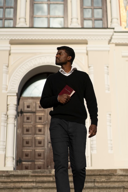 Free photo man holding bible book outside the church