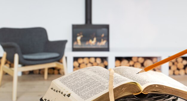 A man holding a Bible with a pencil, against the background of the living room with a fireplace. Reading a book in a cozy environment.