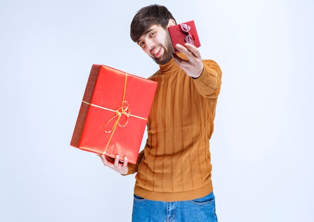 Man holding big and small red gift boxes and offering one of them to his girlfriend.