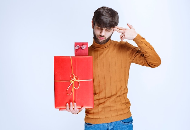 Free photo man holding big and small red gift boxes and thinking.