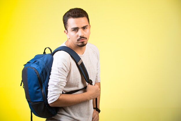 Man holding a blue backpack and looking straight.