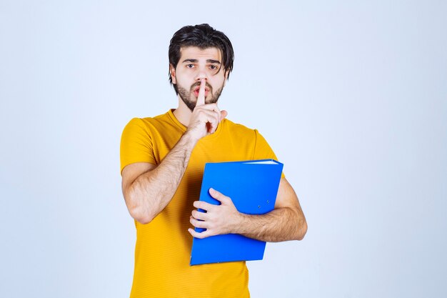 Man holding a blue folder and asking for silence.