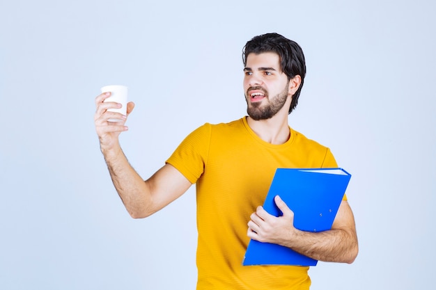 Uomo che tiene una cartella blu e una tazza di caffè.