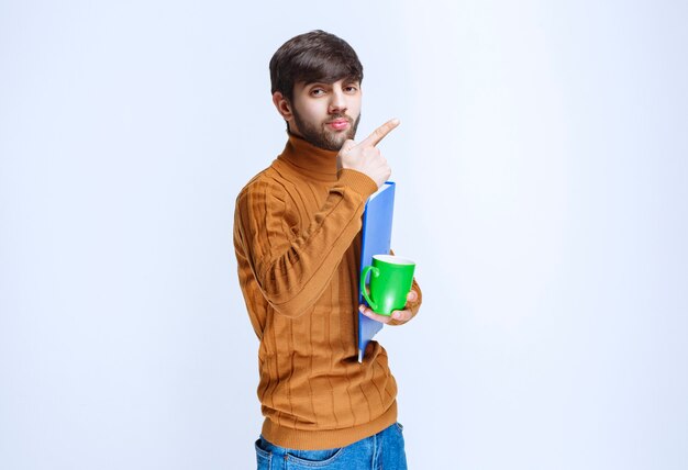 Мужчина держит синюю папку и зеленую чашку напитка.