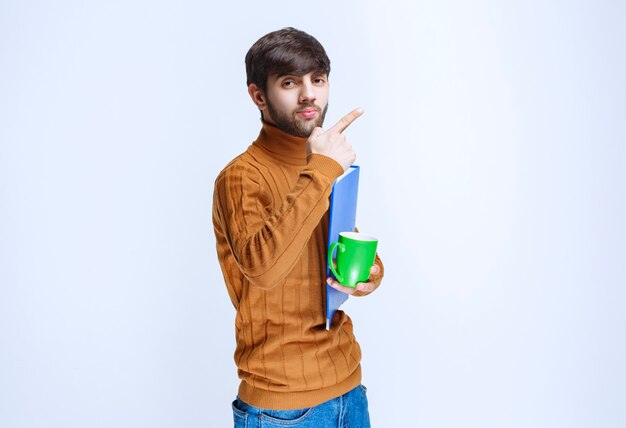 Man holding a blue folder and a green cup of drink.