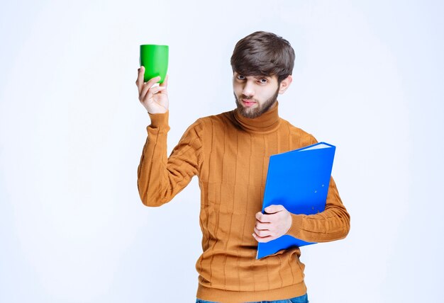 Man holding a blue folder and a green cup of drink.