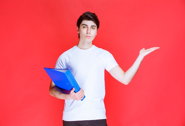 Man holding a blue folder and pointing at somewhere. 