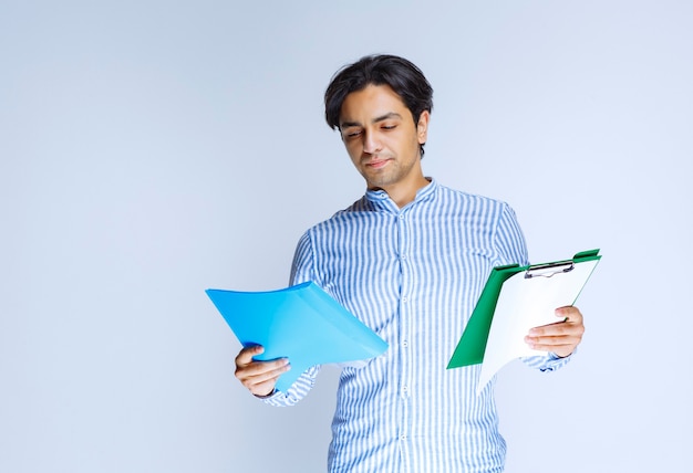 Free photo man holding blue and green report folders and checking them. high quality photo