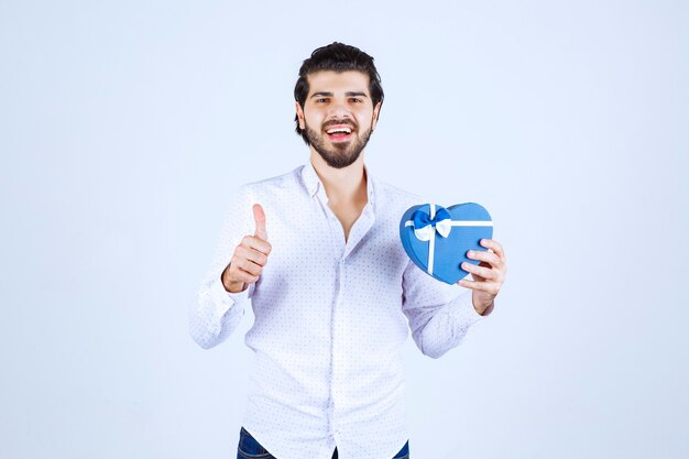 Man holding a blue heart shape gift box and showing thumb up