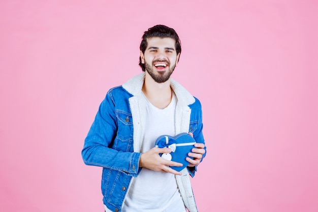 Uomo che tiene in mano una scatola regalo a forma di cuore blu e sembra felice