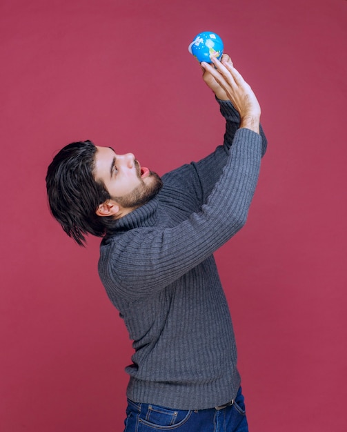 Man holding a blue mini globe and looking at it attentively. 