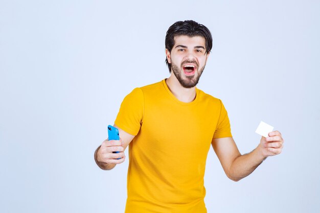 Man holding a blue smartphone and checking his messages or calling the contact number on the business card.