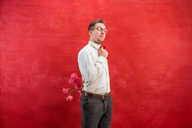 Мужчина держит букет гвоздик за спиной на фоне красной студии