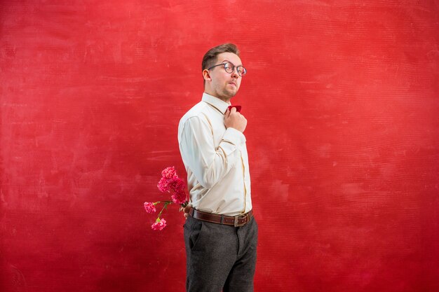 Man holding bouquet of carnations behind back on red studio background