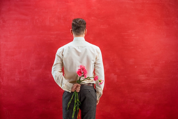 Бесплатное фото Мужчина держит букет гвоздик за спиной на красной студии