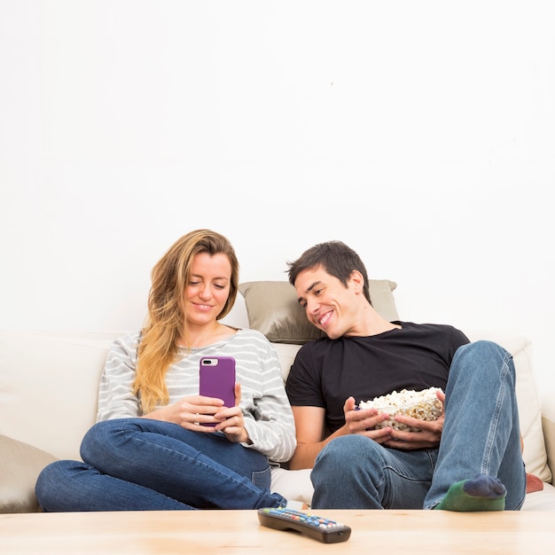 Man holding bowl of popcorns looking at cell phone hold by her girlfriend