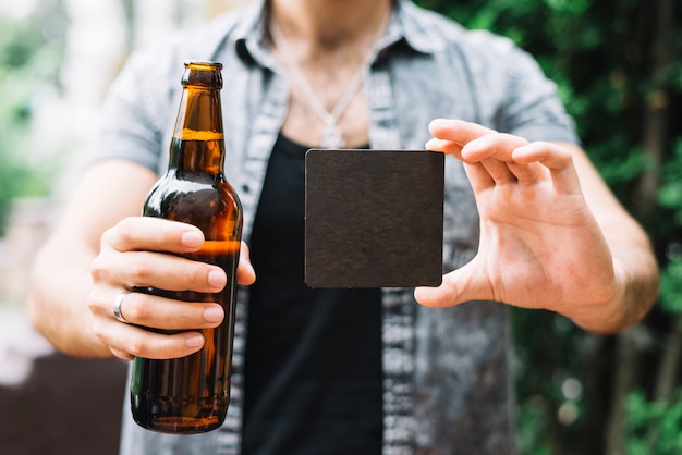 Man holding brown beer bottle and black blank card in hands