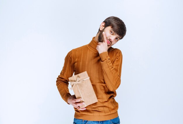 Man holding a cardboard gift box and looks confused and hesitating.