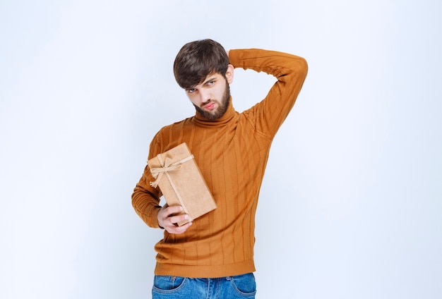 Мужчина держит картонную подарочную коробку и выглядит смущенным и нерешительным.