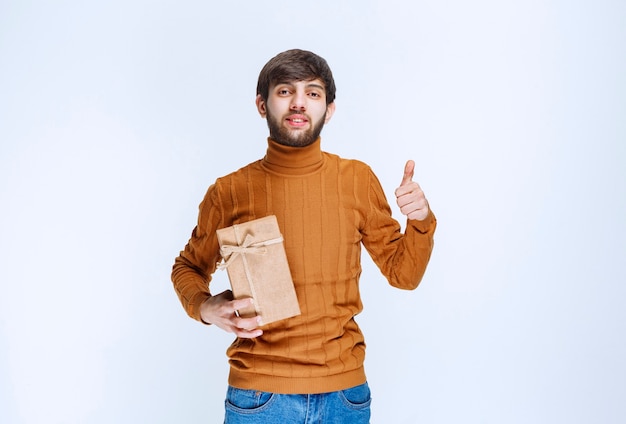 Man holding a cardboard gift box and showing enjoyment sign.