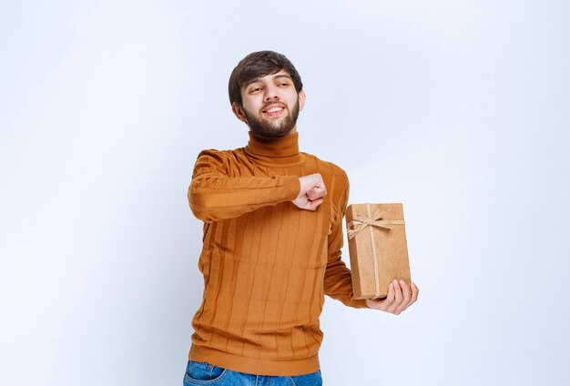 Man holding a cardboard gift box and showing enjoyment sign.