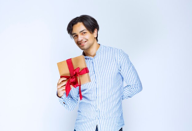 Man holding a cardboard gift box with red ribbon and feeling positive. High quality photo