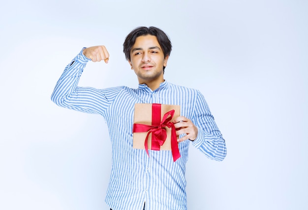 Man holding a cardboard gift box with red ribbon and showing his fist as a successful person. High quality photo