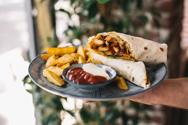 Man holding chicken burrito served with fries mayonnaise and ketchup