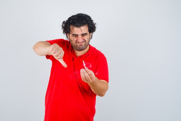 Man holding cigarette, showing thumb down in red t-shirt and looking focused