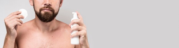 Man holding a cleansing disk and shaving cream bottle