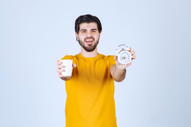 Free photo man holding a coffee cup and alarm clock pointing to morning routine.