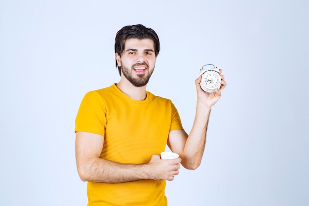 Free photo man holding a coffee cup and alarm clock pointing to morning routine.