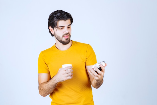 Man holding a coffee cup and alarm clock pointing to morning routine.