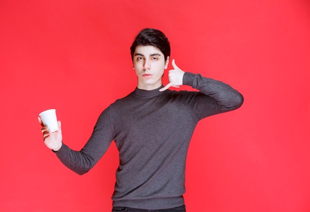 Free photo man holding a coffee cup and making sign to a call