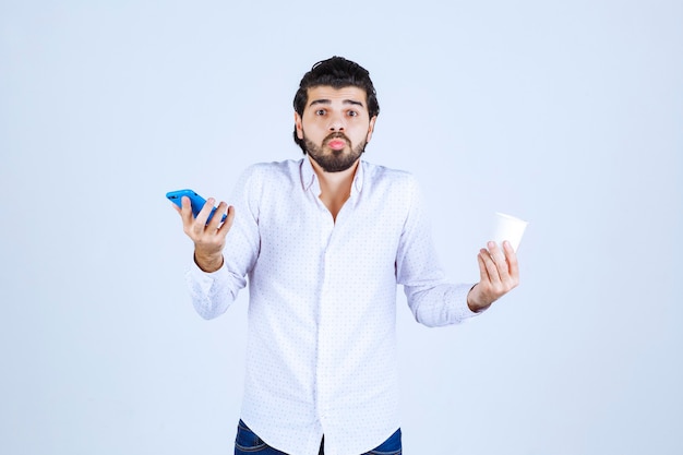 Man holding a coffee cup in one hand and checking his phone in another hand