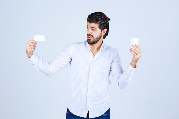 Man holding a coffee cup in one hand and presenting his business card in another hand