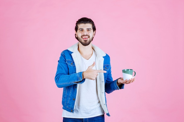 Uomo che tiene una tazza di caffè e che indica a esso.