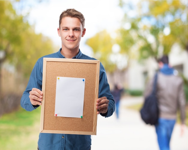 Free photo man holding a cork bulletin board with a blank sheet