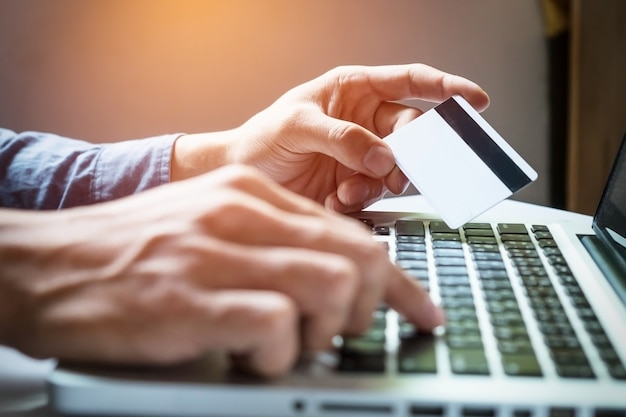 Man holding credit card in hand and entering security code using laptop keyboard