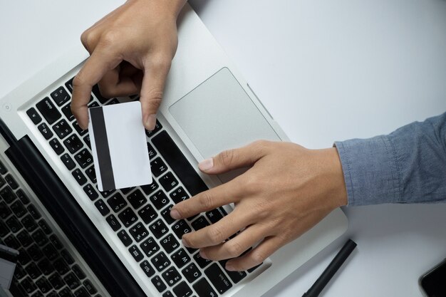 Man holding credit card in hand and entering security code using laptop keyboard