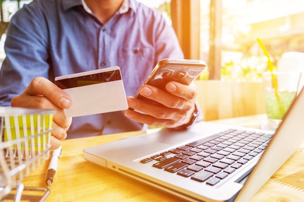 Man holding credit card in hand and entering security code using laptop keyboard.