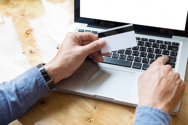 Man holding credit card in hand and entering security code using laptop keyboard.