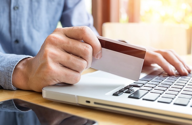 Man holding credit card in hand and entering security code using laptop keyboard.