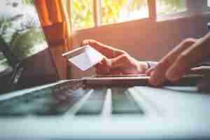Бесплатное фото Мужчина держит кредитную карту в руке и вводит код безопасности с помощью смартфона на клавиатуре ноутбука, концепция онлайн-покупок.