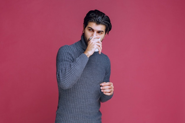 Man holding a disposable coffee cup and drinking it.