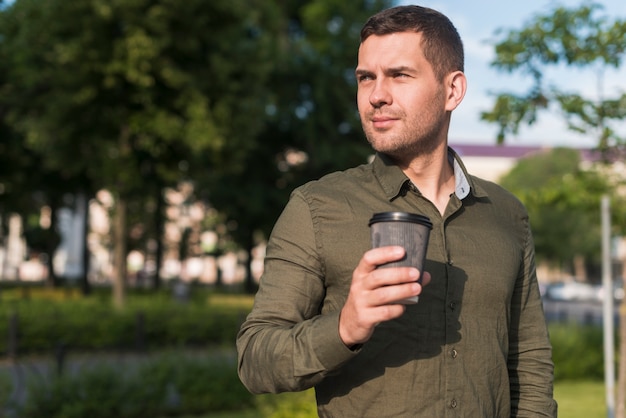 Man holding disposable coffee cup looking away at park