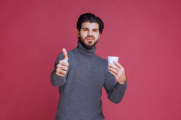 Man holding a disposable coffee cup and makes enjoyment sign.